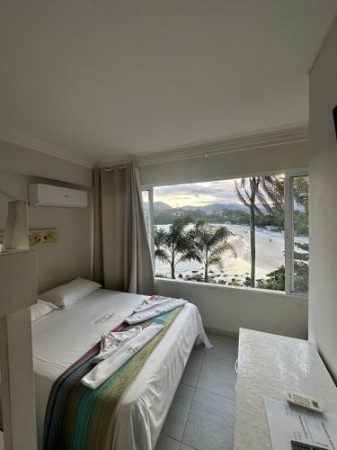a bedroom with a bed and a large window with a beach at Mansão Tenório in Ubatuba