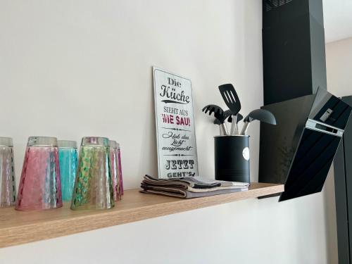 a shelf with several different colored glasses and a book at Zauberhafte Ferienwohnung mit Wellness-Bad in Bad Harzburg