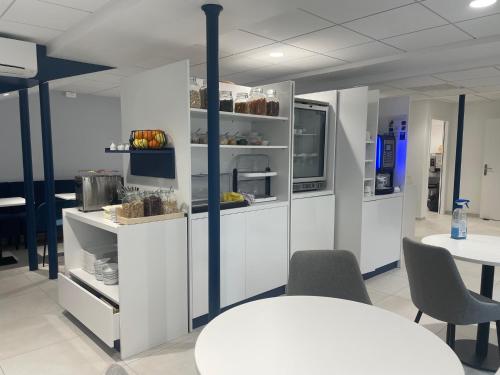 a kitchen with white cabinets and a white table and chairs at Kyriad Saumur Hyper Centre Hôtel Appartements et SPA soins Sothys Paris in Saumur