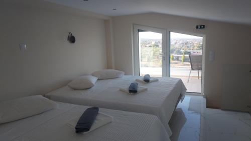 a white bedroom with two beds and a large window at AIR-IN Rooms with magnificent views in Artemida