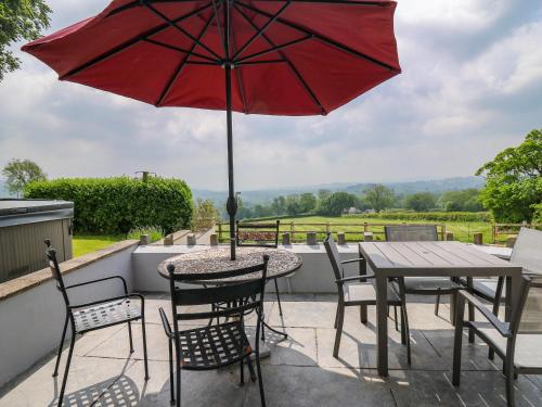 a patio with a table and chairs and a red umbrella at Aberdauddwr in Llanwnen