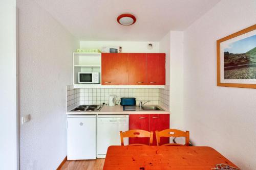 - une petite cuisine avec des placards rouges, une table et des chaises dans l'établissement Résidence Le Hameau des Ecrins - maeva Home - Appartement 2 Pièces 4 Personnes - Confort MAE-6158, à Puy-Saint-Vincent