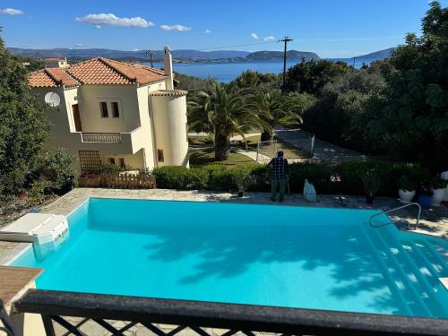 a man standing next to a swimming pool in front of a house at Villa Nova s.r Sea View in Porto Heli