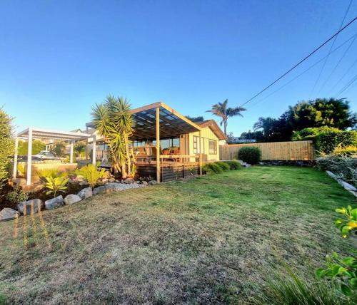 a yellow house with a fence and a yard at Tropical Oasis in Golden Circle in Mangawhai