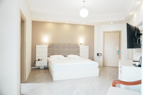 a white bedroom with a large bed and a tv at Hotel Mediterrane in Sarandë