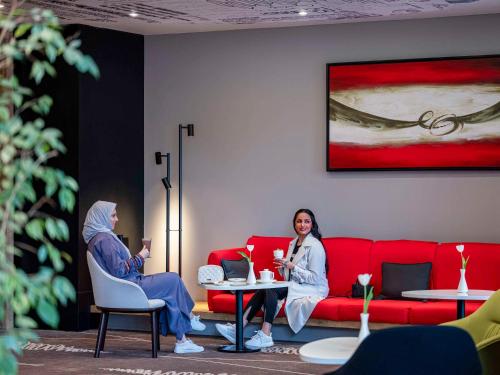 two women sitting in a room with a red couch at Ibis Jeddah Malik Road in Jeddah