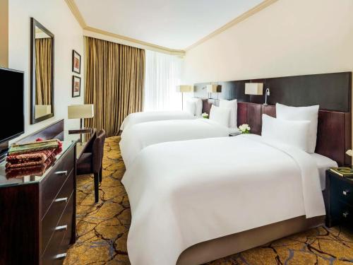 メッカにあるモーベンピック ホテル & レジデンス ハジャル タワー メッカのベッド3台とテレビが備わるホテルルームです。