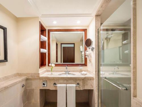 een badkamer met een wastafel, een spiegel en een bad bij Movenpick Makkah Hajar Tower in Mekka