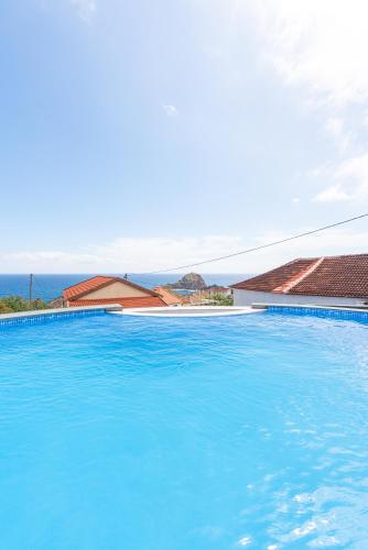 a large blue swimming pool with the ocean in the background at Lighthouse view- POOL VILLA in Porto Moniz
