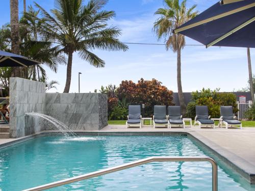 a pool with chairs and an umbrella and palm trees at Boulevard Towers on Broadbeach in Gold Coast