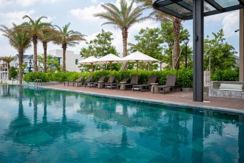 a swimming pool with chairs and palm trees at AnnA Villa - Novaworld Phan Thiết in Bình Tú