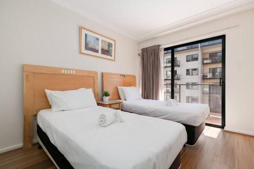 two beds in a hotel room with a window at 2X1 Comfy Apartment in Perth CBD in Perth