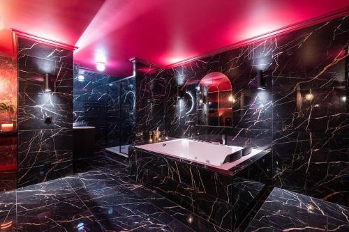 une salle de bain noire avec une baignoire et un éclairage rose dans l'établissement L'Evidence, à Magny-le-Hongre
