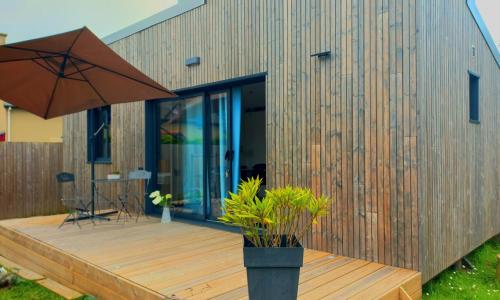 ein Haus mit einer Holzterrasse mit einem Sonnenschirm in der Unterkunft Le p’tit tram in Cancale