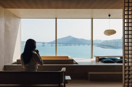 a woman sitting on a bench looking out at the water at ONUJI stay in Busan