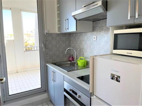 une cuisine avec un évier et un micro-ondes dans l'établissement Appartement 1 chambre en bord de mer, 34m² d’extérieurs, parking privé, La Grande Motte - FR-1-790-22, à La Grande Motte