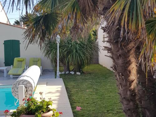 une cour avec un palmier et une piscine dans l'établissement Maison avec Piscine Chauffée, Proche Plage, 3 Chambres, Jardin Clôturé, Wifi Inclus à St Hilaire de Riez - FR-1-652-44, à Saint-Hilaire-de-Riez