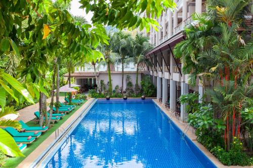 a swimming pool in front of a building with lounge chairs at Thanthip Beach Resort Patong in Patong Beach