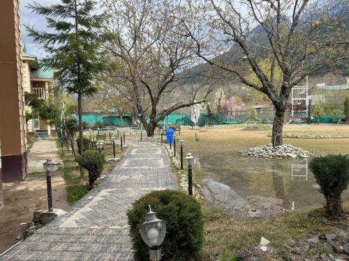 a walkway in a park with trees and a pond at Lidder view Resorts in Pahalgām