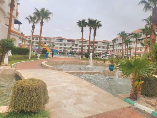 a fountain in a park with palm trees and a building at Garden Beach 2 sidi rahal in Sidi Rahal