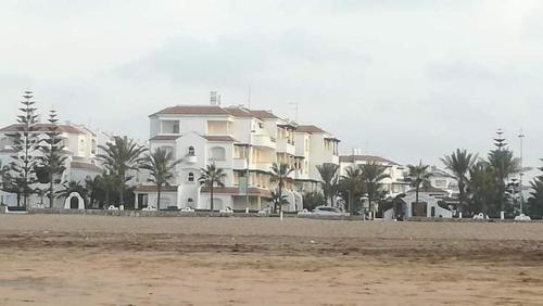 a large white building on the beach with palm trees at Garden Beach 2 sidi rahal in Sidi Rahal
