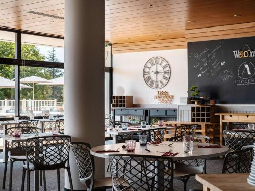 a restaurant with tables and chairs and a clock on the wall at Mercure Toulouse Aéroport Golf de Seilh in Seilh