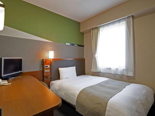 富山市にあるコンフォートホテル富山駅前のベッド、デスク、窓が備わるホテルルームです。