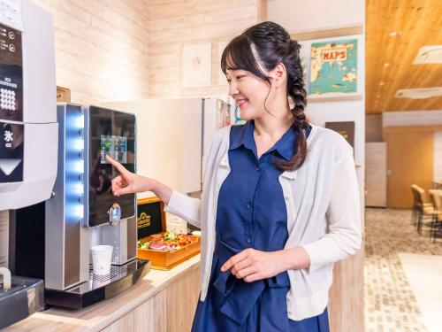 富山市にあるコンフォートホテル富山駅前の女がコーヒーマシンを指している