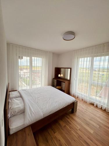 a white bedroom with a bed and two windows at Holiday Apartments Gjakova in Gjakove
