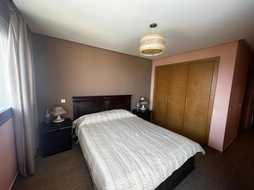 a bedroom with a bed and a wooden cabinet at Luxueux Appartement Plage des Nations in Sidi Bouqnadel