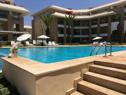 a swimming pool in front of a building at Luxueux Appartement Plage des Nations in Sidi Bouqnadel