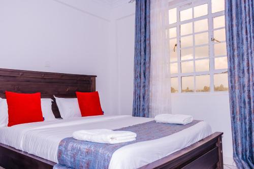 a bedroom with a bed with red pillows and a window at The pine 1 bedroom house California plaza in Nanyuki