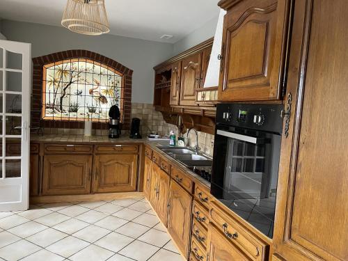 a kitchen with wooden cabinets and a black appliance at Maison coeur des Weppes La Maralbique in Wavrin