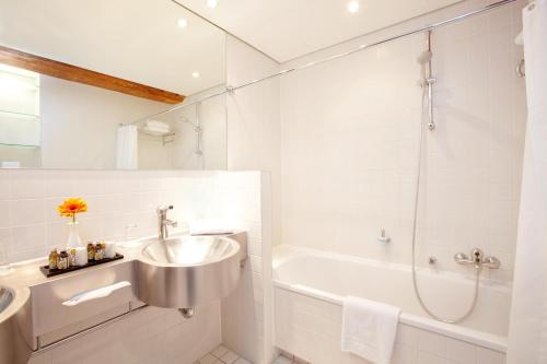 a white bathroom with a sink and a tub at Vienna House by Wyndham Havelufer Potsdam in Potsdam