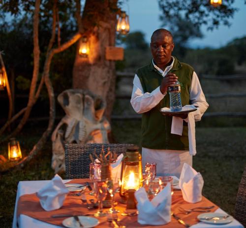 a man standing in front of a table with a bottle at Neptune Mara Rianta Luxury Camp - All Inclusive. in Masai Mara