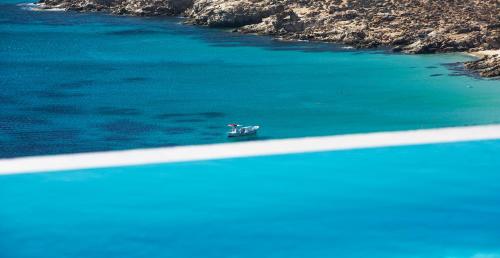 a boat in the water next to a road at Myconian Utopia Relais & Chateaux in Elia Beach
