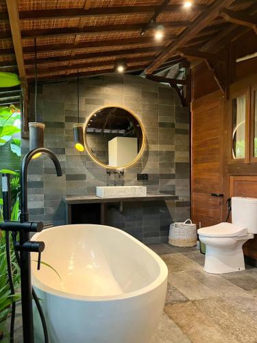a bathroom with a tub and a toilet and a mirror at Kaiwatu House in Ubud