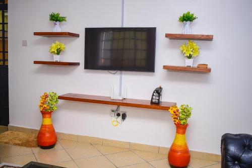 two vases with flowers in them in front of a tv at House of Grace Nakuru Naka Area Airbnb in Nakuru