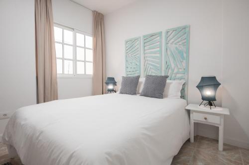 une chambre blanche avec un grand lit blanc et deux lampes dans l'établissement Comfortable Centric Apartment Steps from the Beach, à Gran Tarajal