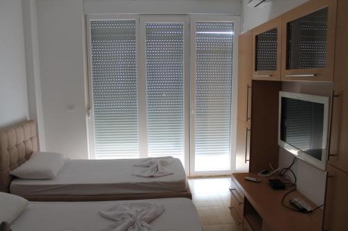 a bedroom with two beds and a television and windows at Blue Apartments & Hotel Shengjin in Shëngjin