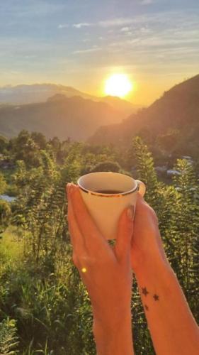 a woman holding a cup of coffee with the sunset in the background at Lush In Ella in Ella