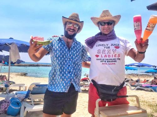 two men are standing on the beach with a sign at Nissi 3 Pool View 2 Bedroom Apartment with Large Veranda in Ayia Napa