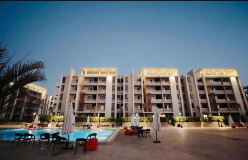 ein großes Apartmenthaus mit Pool, Stühlen und Sonnenschirmen in der Unterkunft Chalet Grand Hills North coast in Dawwār al Ḩajj Aḩmad