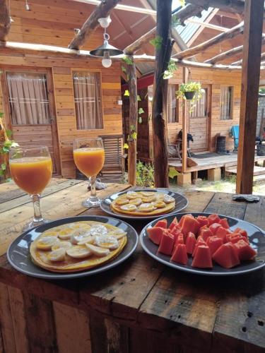 a wooden table with plates of food and two glasses of juice at Silaa Cabana in Trincomalee