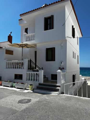 ein weißes Haus mit einem Sonnenschirm vor dem Meer in der Unterkunft Pansion Giannis Perris in Kokkari