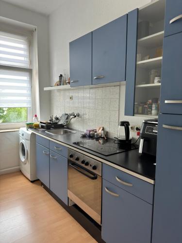 La cuisine est équipée de placards bleus, d'un évier et d'un lave-vaisselle. dans l'établissement Cozy room in Central Dortmund, à Dortmund