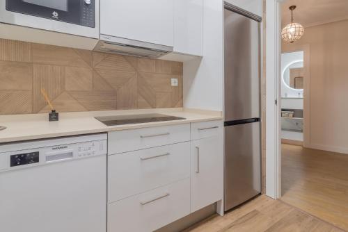 uma cozinha com armários brancos e um frigorífico de aço inoxidável em Apart El Muelle Centro de Ribadesella VUT-3752-AS em Ribadesella