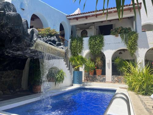 a swimming pool in front of a house with a fountain at Villa de La Roca in Zihuatanejo