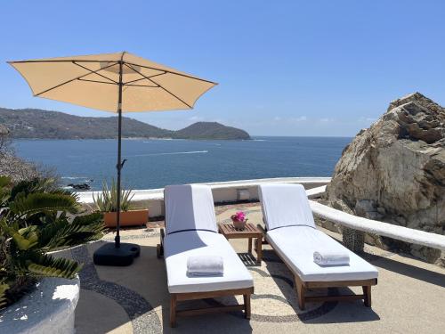 two chairs and an umbrella on a patio with the ocean at Villa de La Roca in Zihuatanejo
