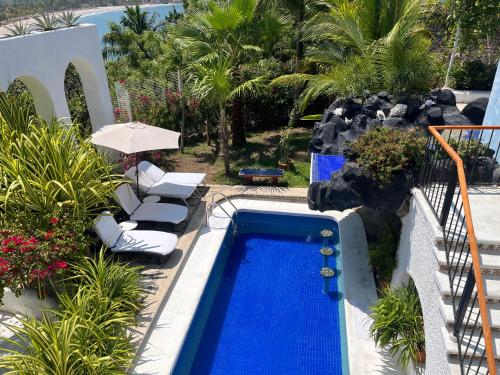 a swimming pool with two chairs and an umbrella at Villa de La Roca in Zihuatanejo